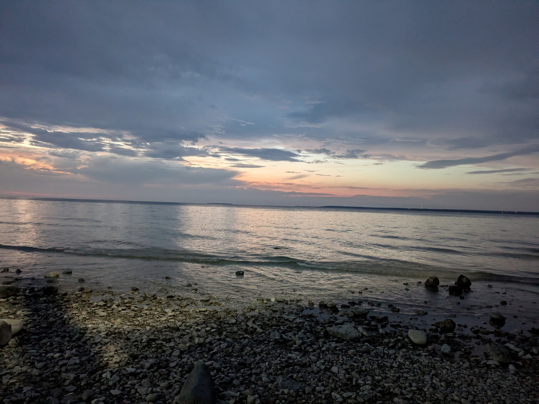 Auto-generated description: A rocky shoreline is captured at dusk, with a tranquil sea and a sky painted in hues of blue and orange.